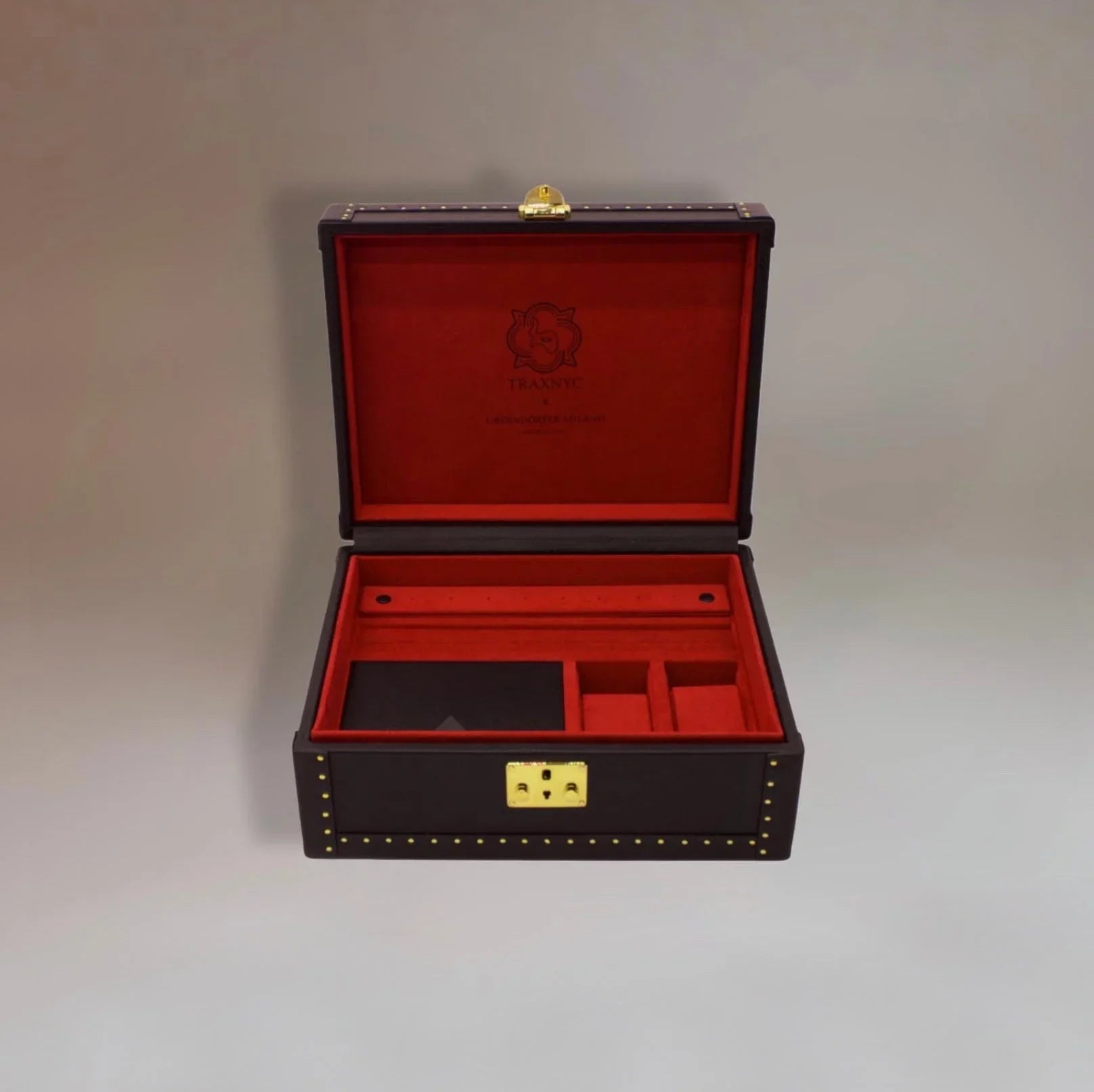 Open luxury leather jewelry box with red velvet interior and gold hardware compartments