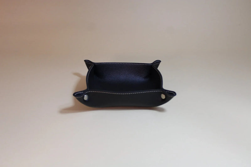Black leather valet tray with white stitching on a neutral background