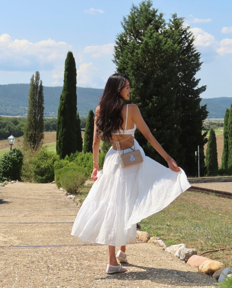 Woman in a white dress standing outdoors with trees and mountains in the background