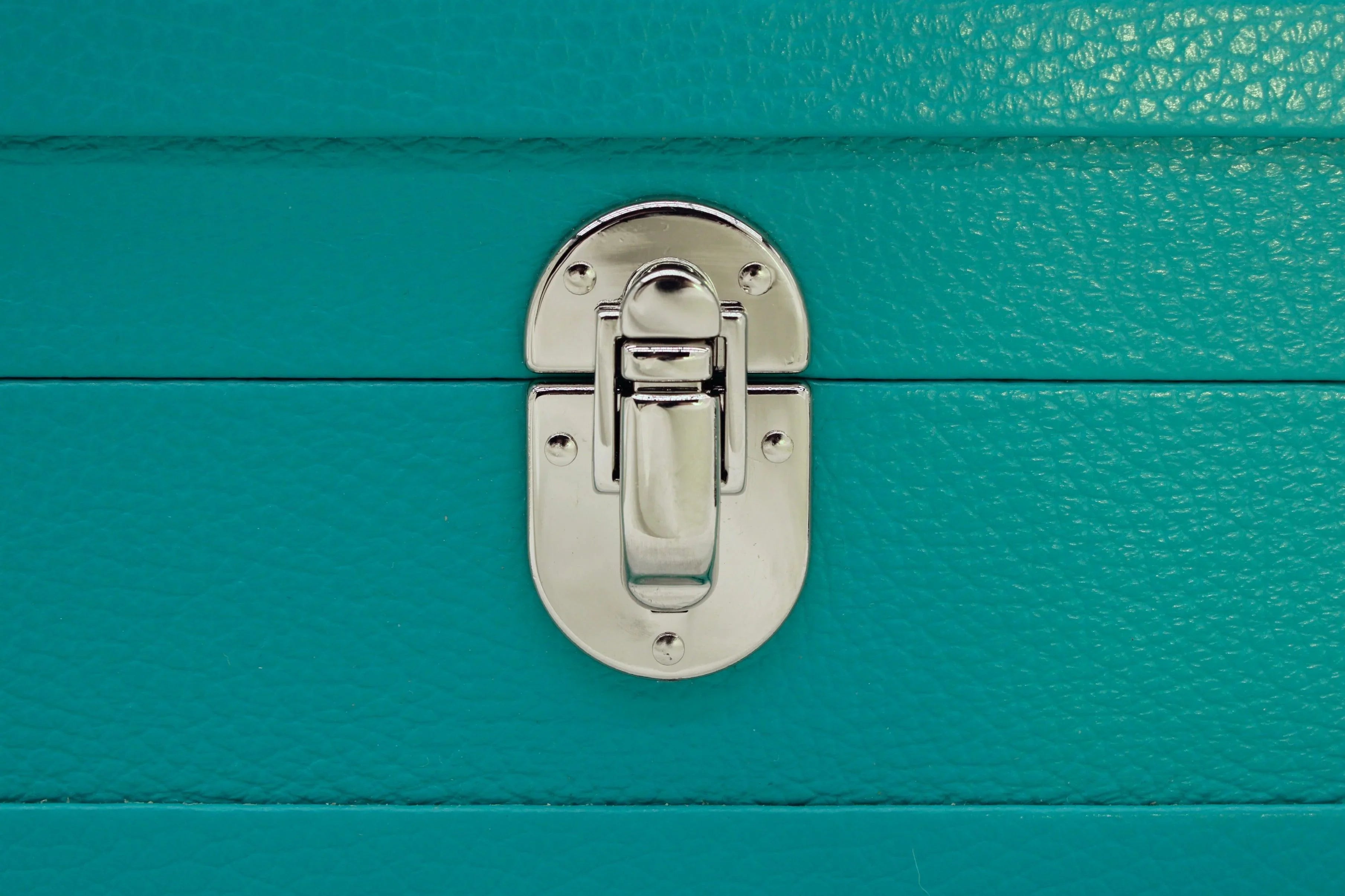 Close-up of silver clasp on turquoise textured leather case, luxury accessory detail