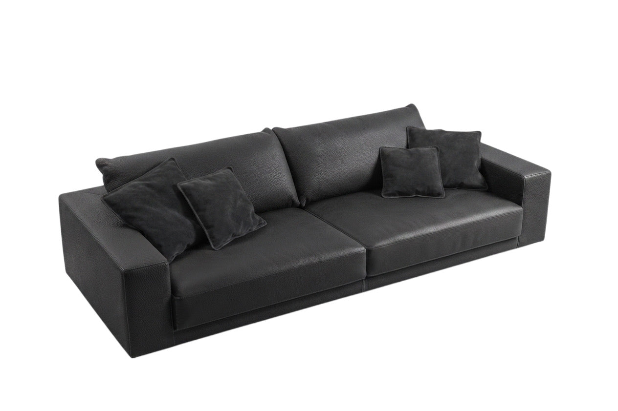 A modern two-seater sofa upholstered in black leather, featuring four matching black throw pillows, shown from a three-quarters angle on a plain white background.