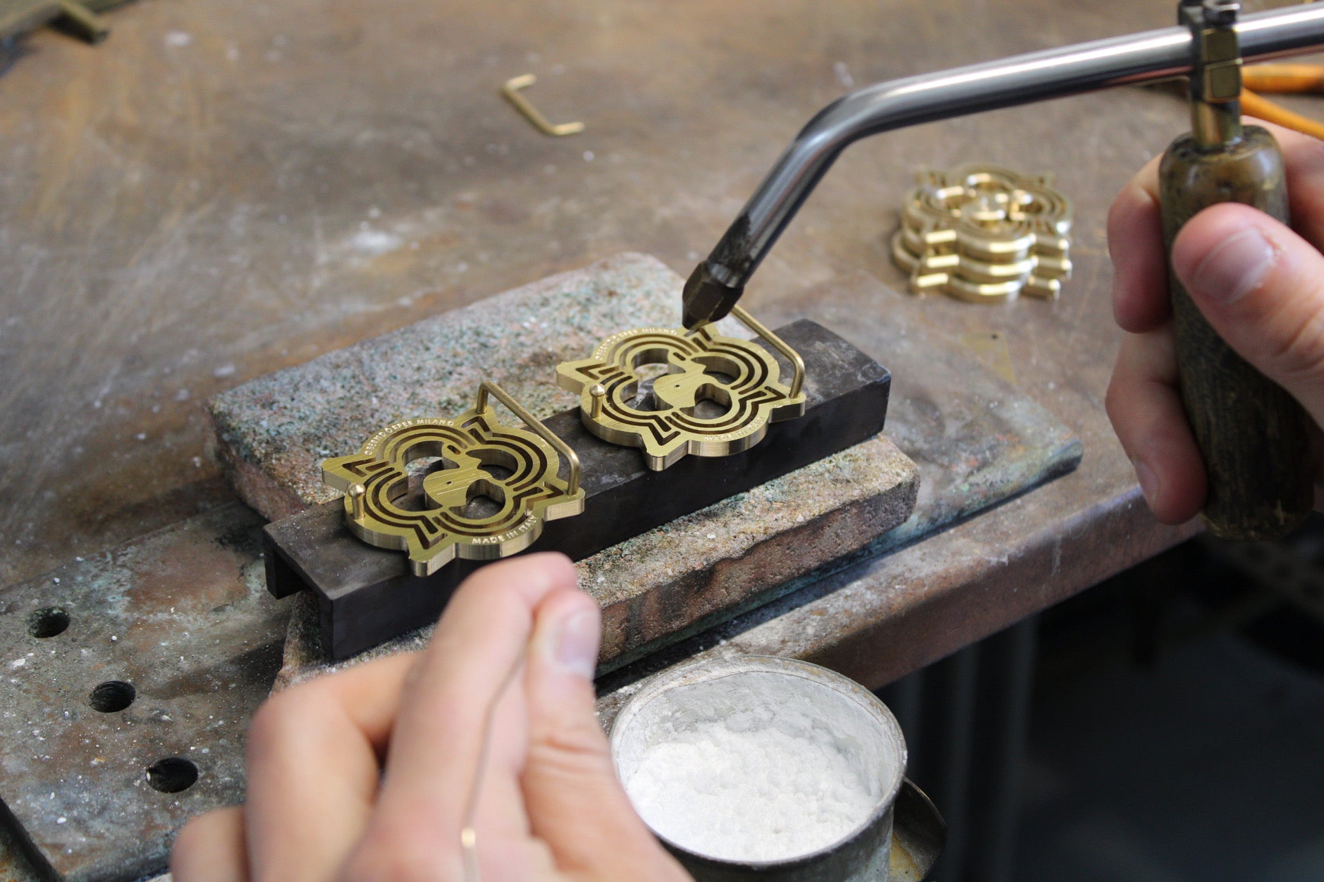 Person working with brass components on a metal surface using a torch.