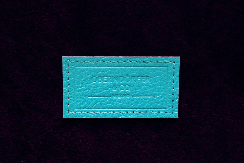 Turquoise leather label with embossed text on dark background, luxury Italian craftsmanship