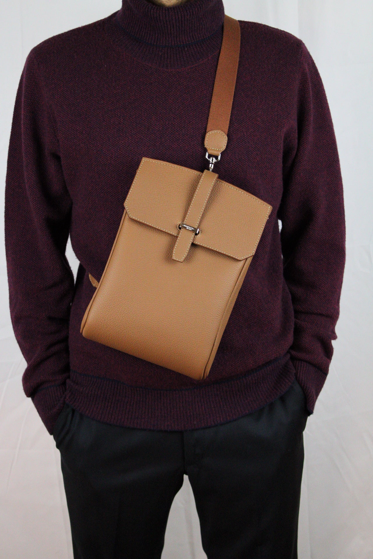 Brown leather bag with a strap over a sweater on a white background