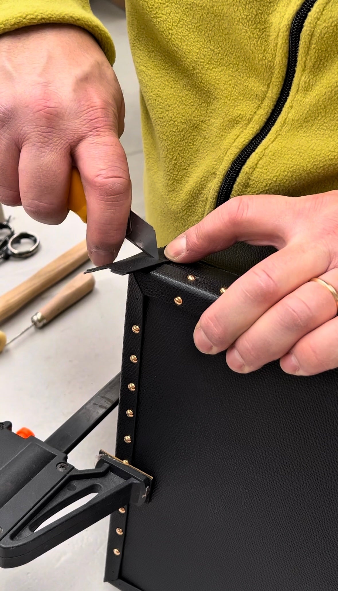 Person using a tool on a black leather item with tools in the background