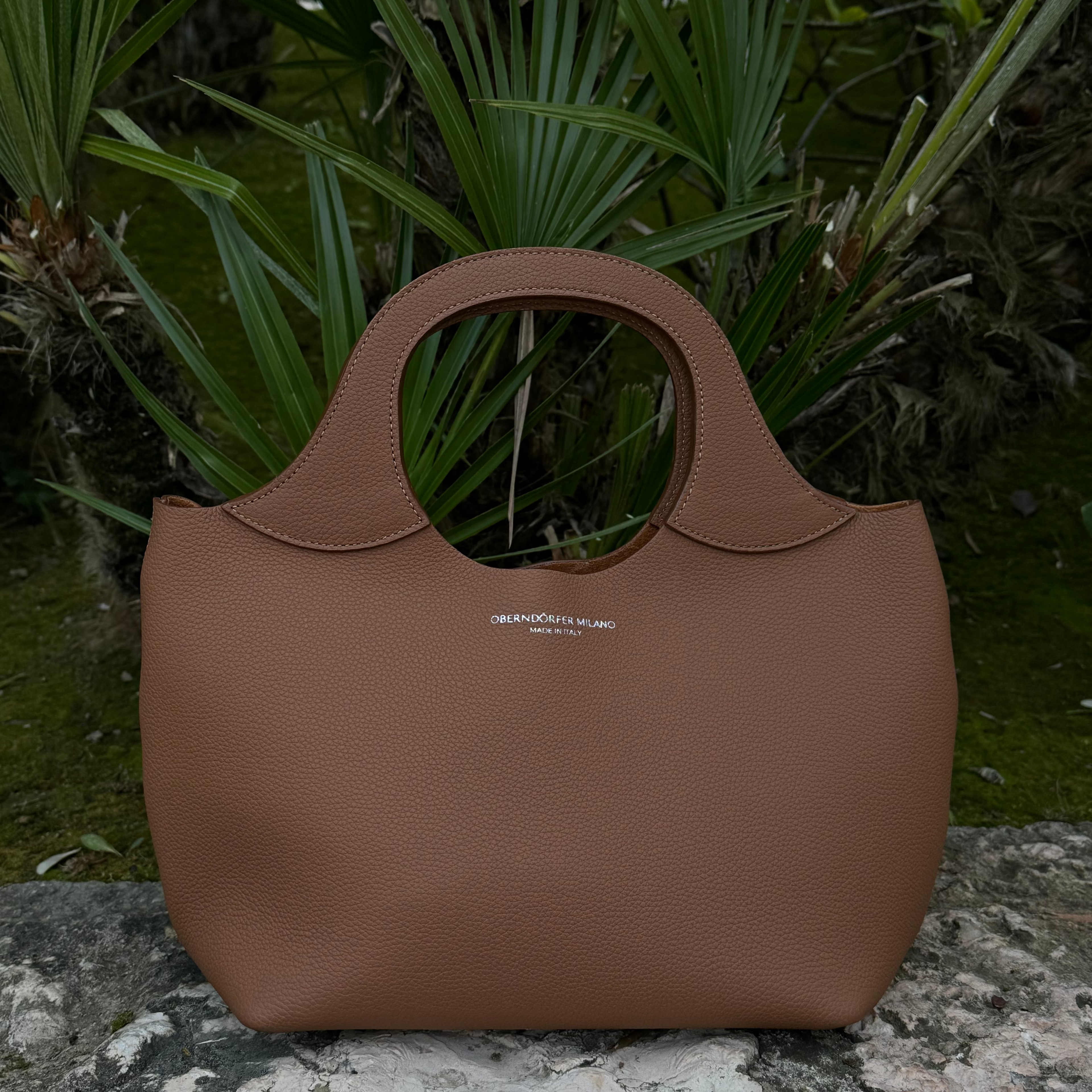 Brown handbag on a stone surface with green foliage in the background
