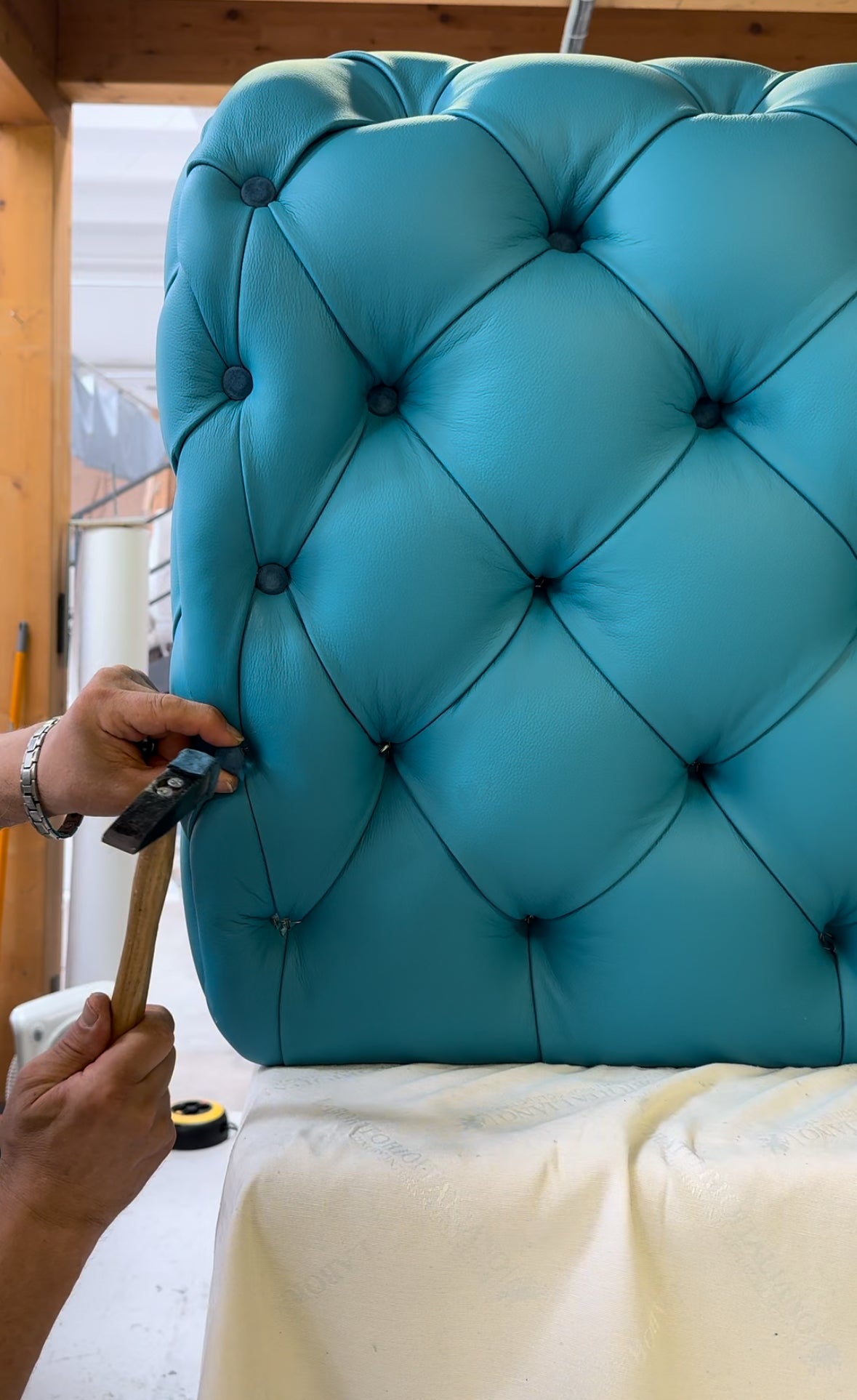 Setting the buttons of a tufted turquoise leather backrest by hand in the atelier