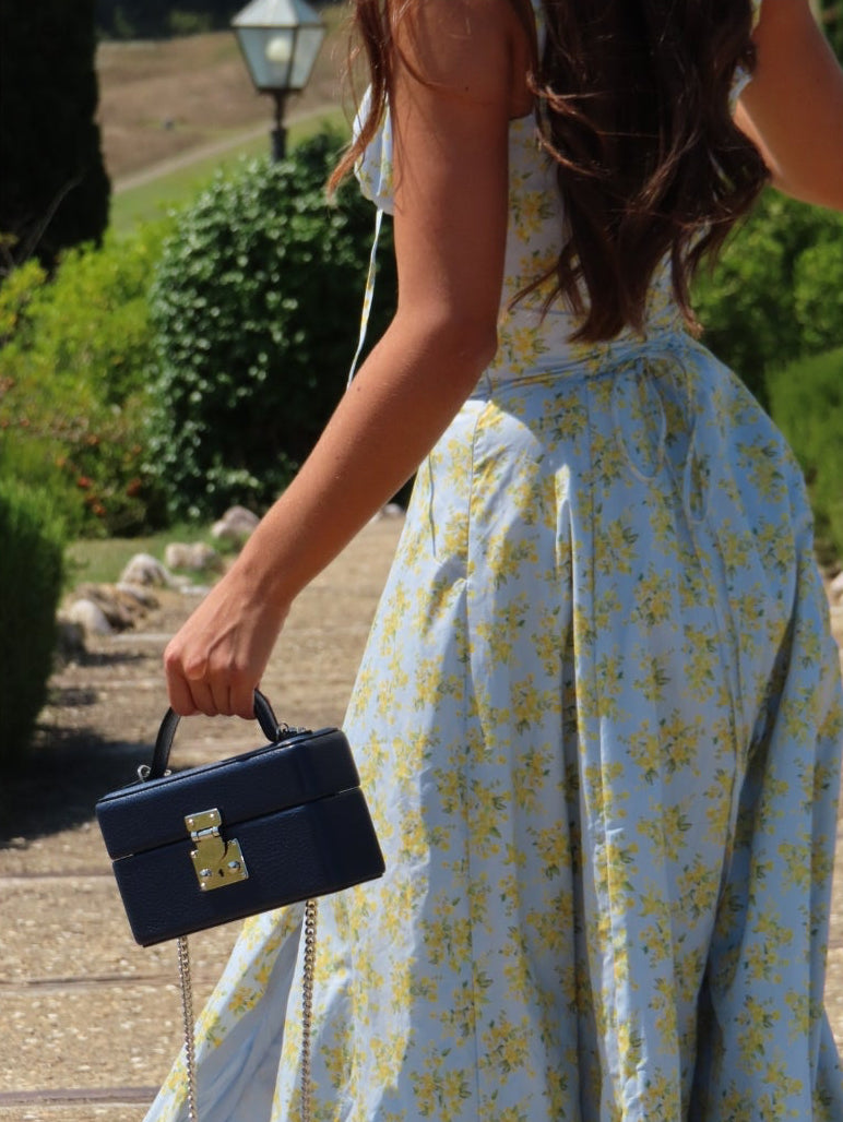 Person wearing a light blue floral dress holding a black handbag in an outdoor setting.