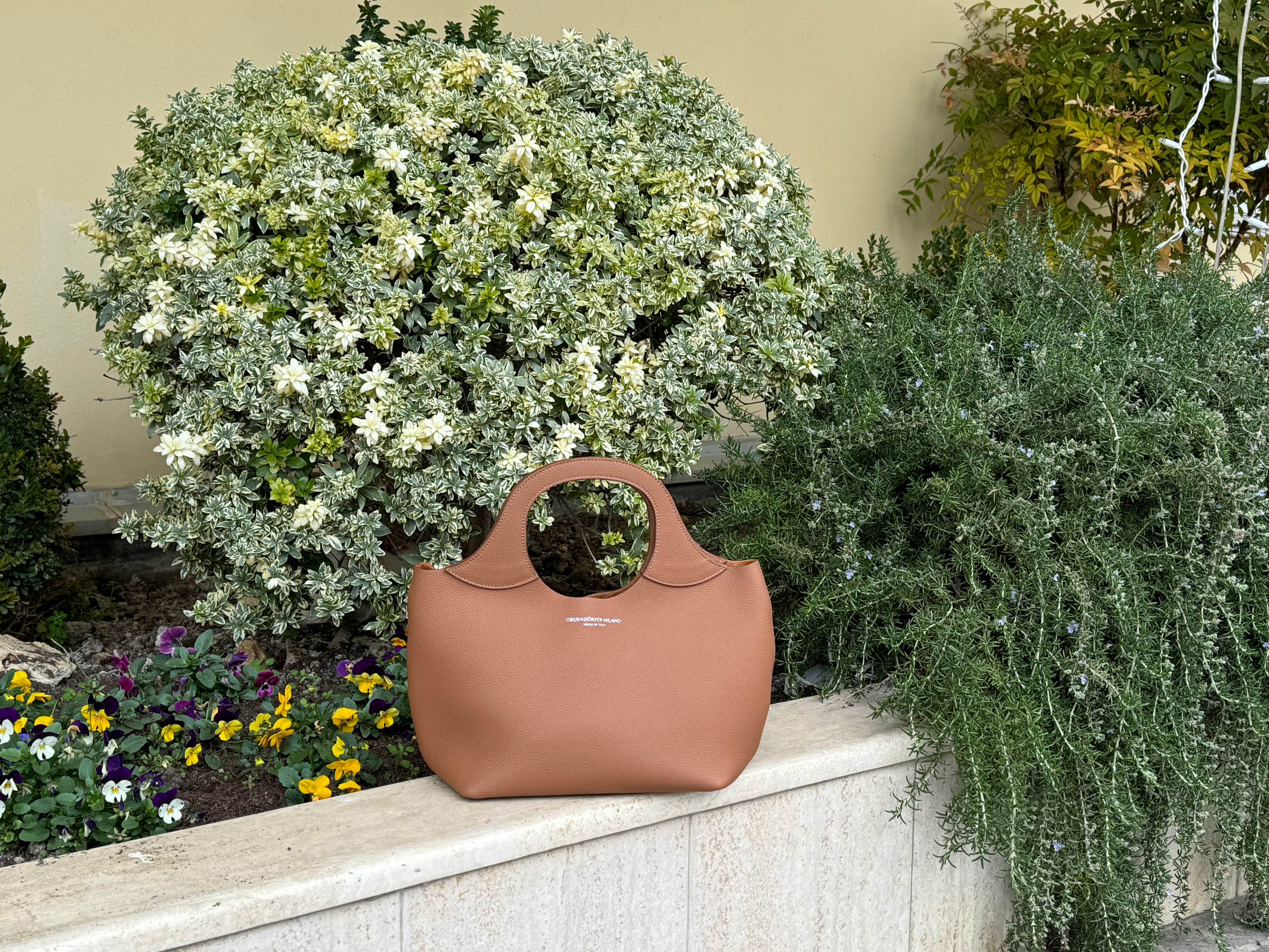 Brown handbag on a ledge with greenery and flowers in the background