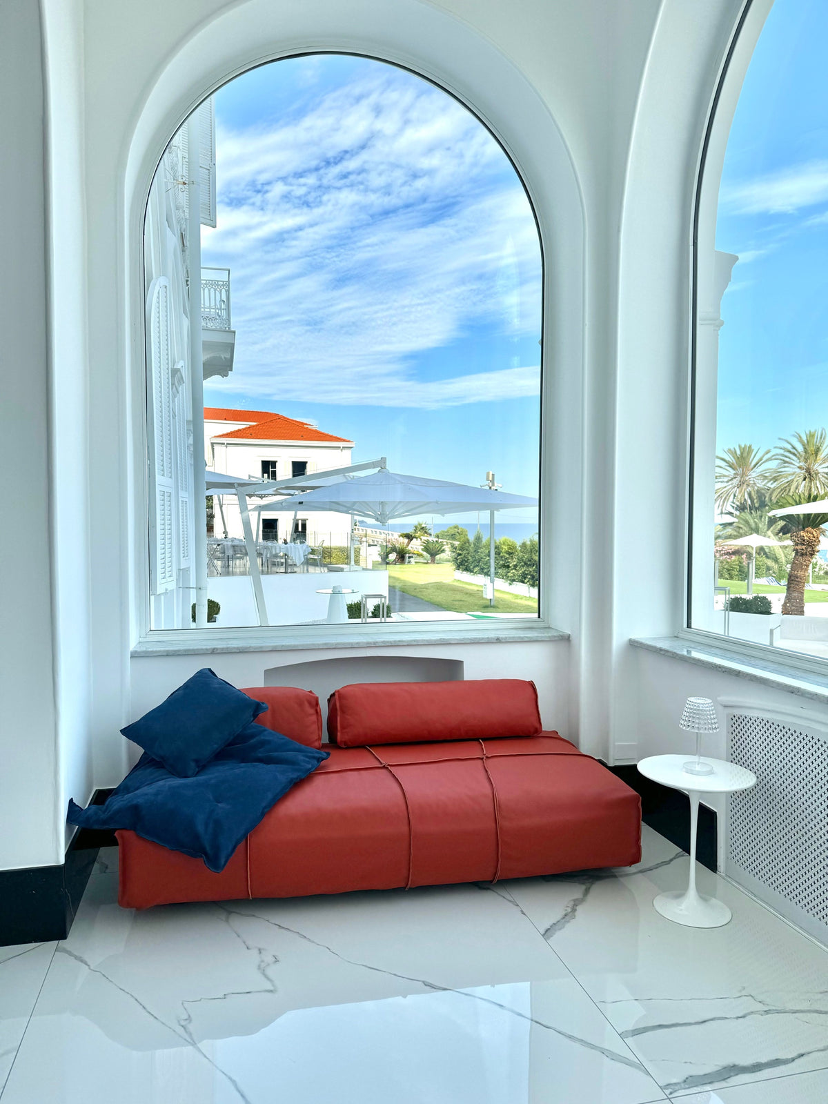 Red leather daybed beneath an arched window overlooking the Ligurian sea
