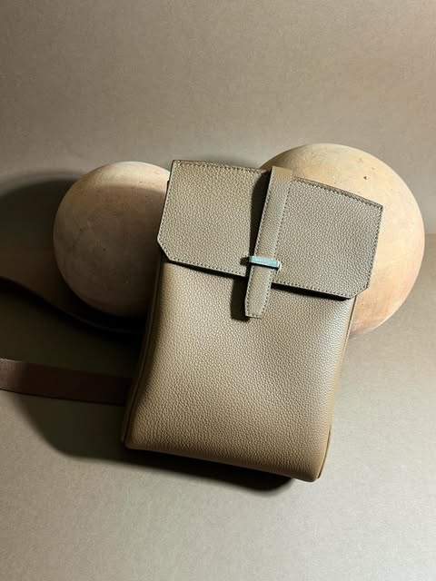 Taupe leather crossbody bag resting on terracotta spheres, staged studio still life