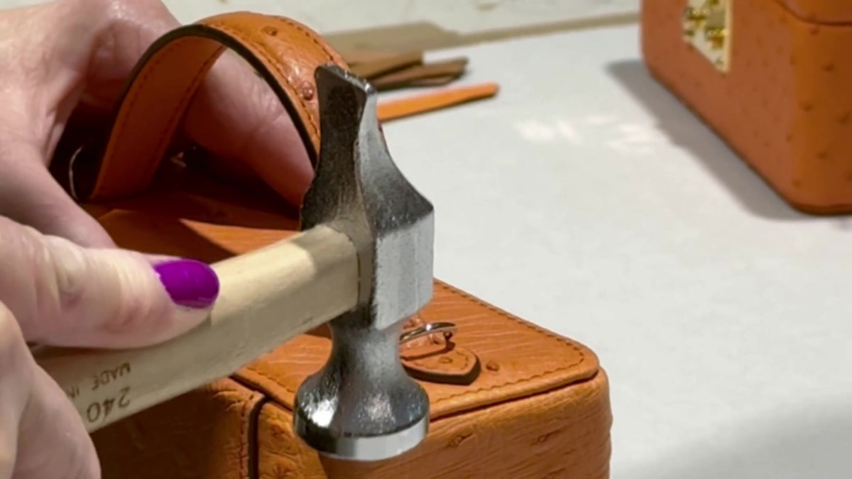 The handle of an orange ostrich trunk handbag hammered on by hand