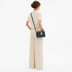 A model from behind wearing a cream short-sleeve top and matching wide-leg trousers, carrying a small black textured crossbody bag with a silver clasp.